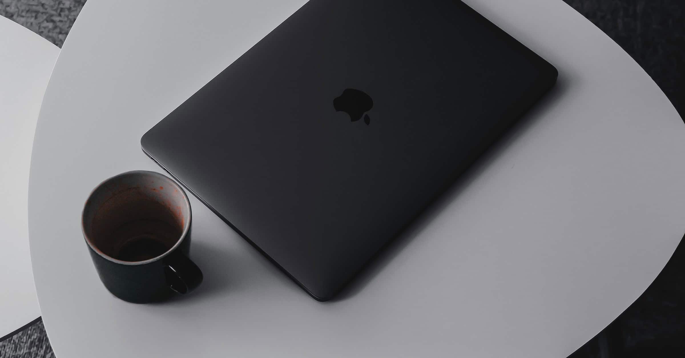laptop with recognizable brand on table with coffee mug