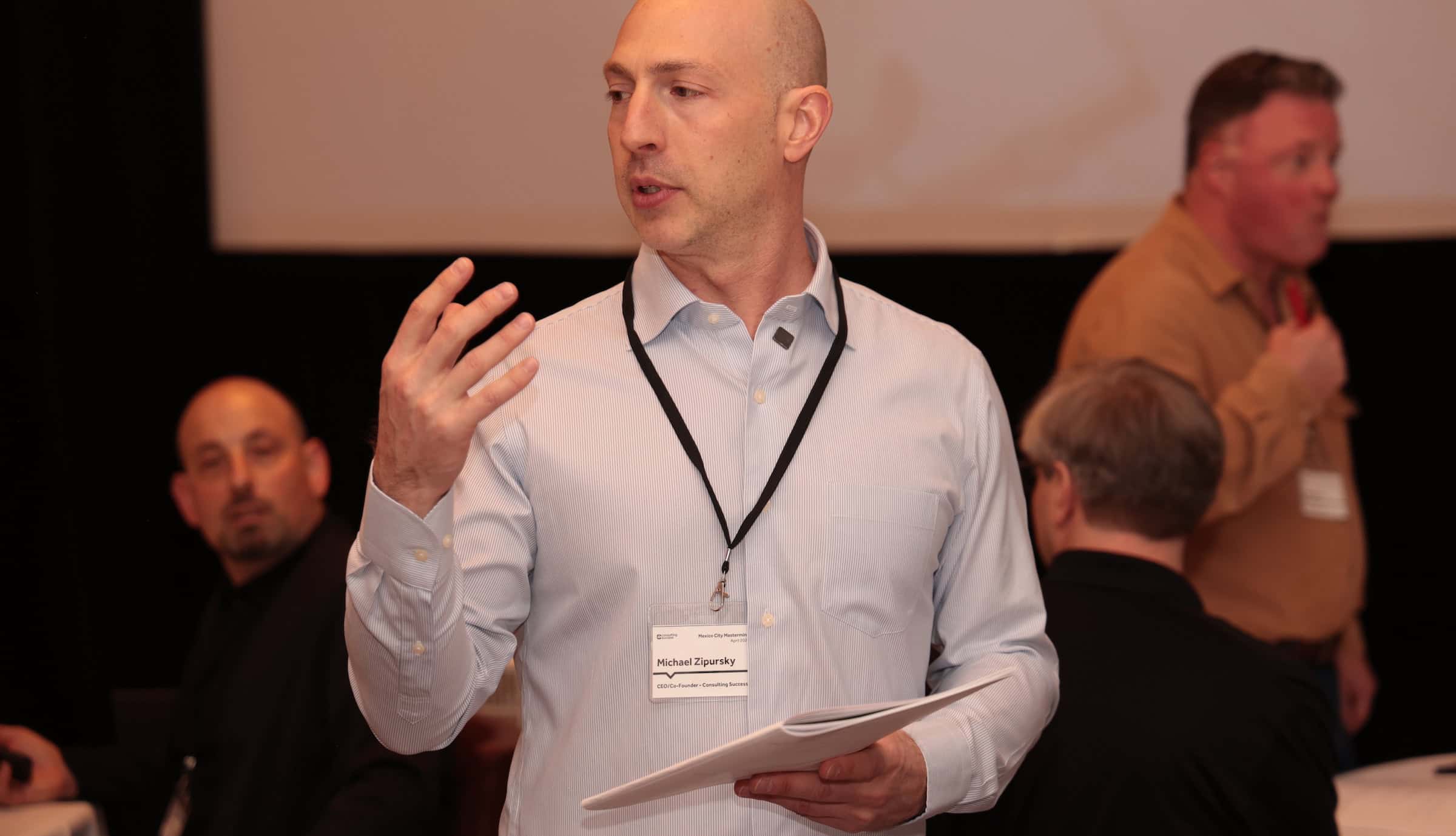 Michael, CEO of Consulting Succcess presents complete consulting marketing strategy guide to a room of consultants.