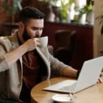Where Your Best Thinking Actually Happens A bearded consultant working on a laptop in a quiet coffee shop, sipping coffee and focusing on deep work and strategic thinking in a relaxed, productive environment.