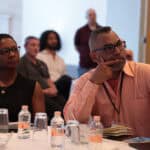 Established consulting founders listening intently during a session at a Consulting Success mastermind retreat, one resting his chin on his hand in thought.