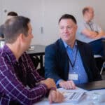 How to Set a Consulting Hourly Rate (And What To Do Instead) Two men in a meeting share conversation at a table with papers and a laptop nearby.